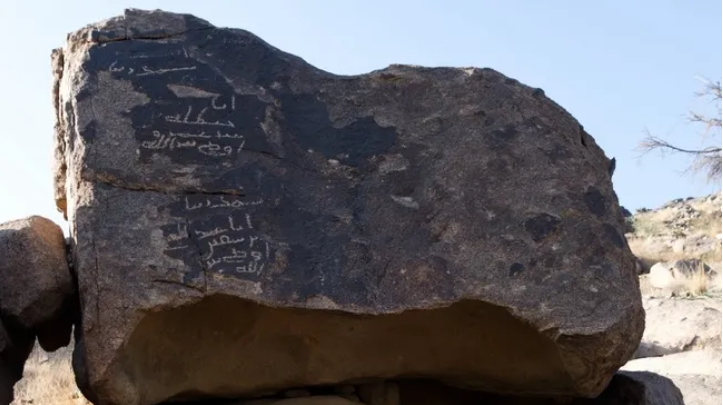 Batu besar dengan dua prasasti Paleo-Arab. Prasasti paling atas kemungkinan diukir oleh Ḥanẓalah bin Abī ʿĀmir, seorang sahabat Muhammad.