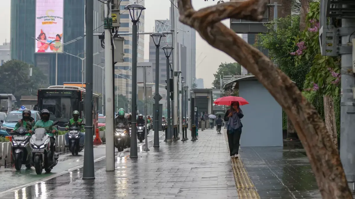 Sejumlah pejalan kaki melindungi diri dengan payung dan jaket saat hujan turun di sekitar Bundaran HI, Jakarta, Selasa (28/10/2025). (Hanung Hambara/Jawa Pos)