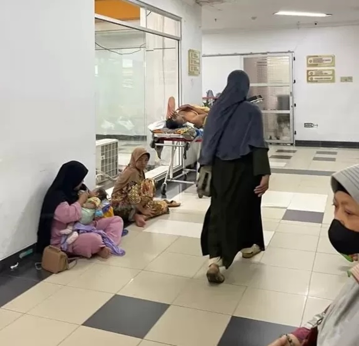 KP ANTRE LAMA. Seorang pasien menggendong anaknya duduk melantai sambil menunggu antrean layanan kesehatan rawat jalan di RSUD IA Moeis.