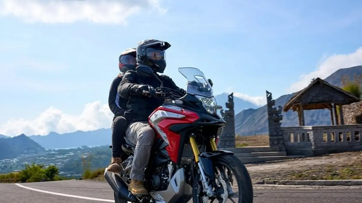 Dua pengendara melaju dengan sepeda motor bergaya adventure di jalan berliku dengan latar pegunungan, menikmati perjalanan yang aman dan nyaman di tengah pemandangan alam yang indah