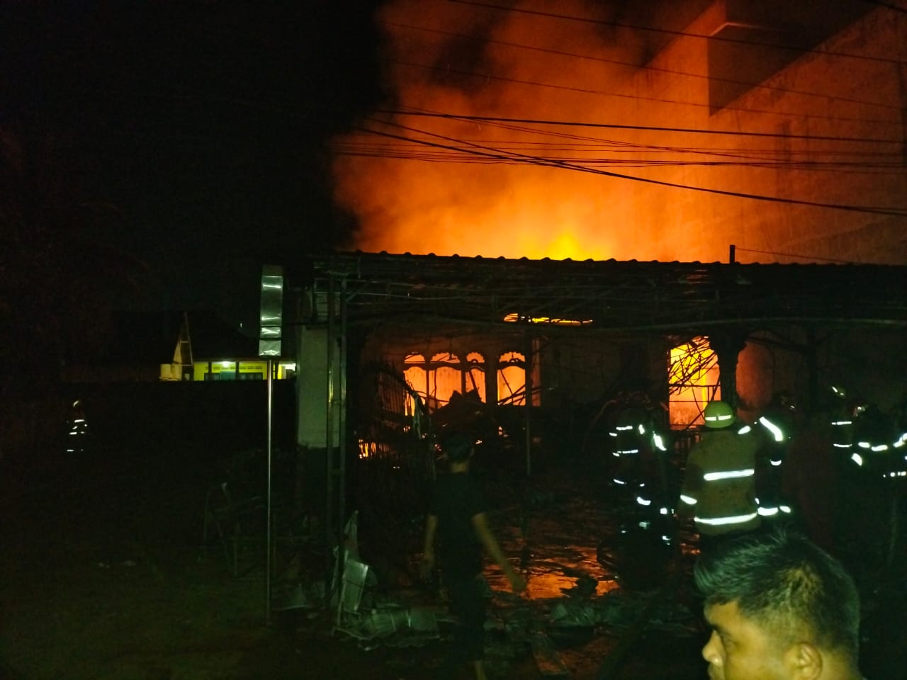 Petugas kepolisian dan pemadam kebakaran dibantu warga saat berupaya memadamkan api.