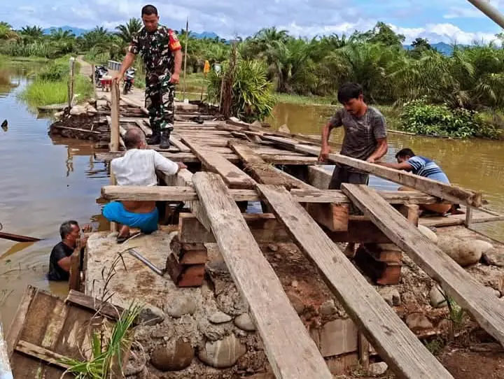 Masyarakat bersama TNI gotong royong bersama memperbaiki jembatan yang rusak akibat sungai meluap dan banjir di Desa Tambahan Nanjur.