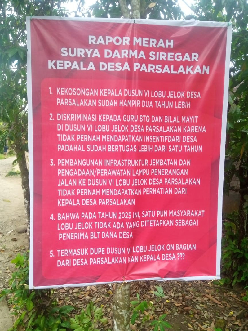 Spanduk bertuliskan &lsquo;Rapor Merah Surya Darma Siregar Kepala Desa Parsalakan&rsquo;.