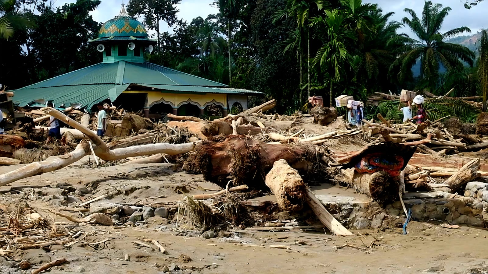 Penyintas menyeberangi sisa banjir di antara sisa bangunan masjid pinggir sungai Aek Garoga, Desa Garoga, Kecamatan Batangtoru, Kabupaten Tapanuli Selatan, Sabtu (29/11/2025). (Samman/MetroDaily)