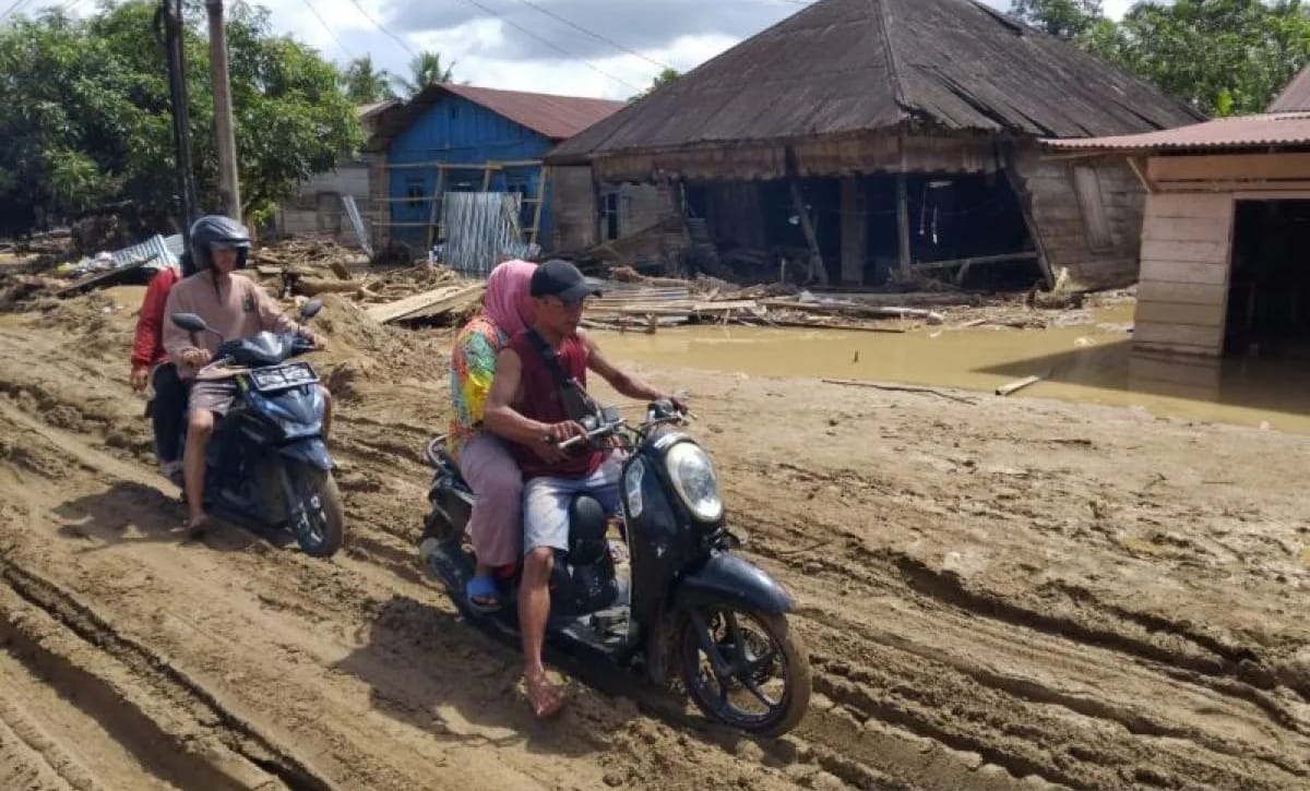 Pengendara sepeda motor memaksa melintas di Jalan Lintas Sumatera yang berlumpur setelah terseret banjir bandang di Desa Garoga, Kecamatan Batang Toru.