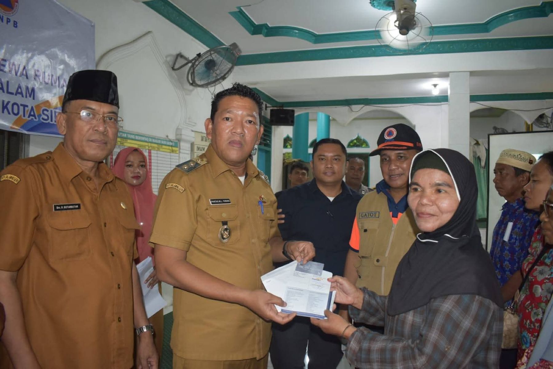 Wakil Wali Kota Sibolga Pantas Maruba Lumban Tobing menyerahkan Dana Tunggu Hunian (DTH) kepada 34 Kepala Keluarga korban bencana di Masjid Budi Sehati, Selasa (30/12/2025).