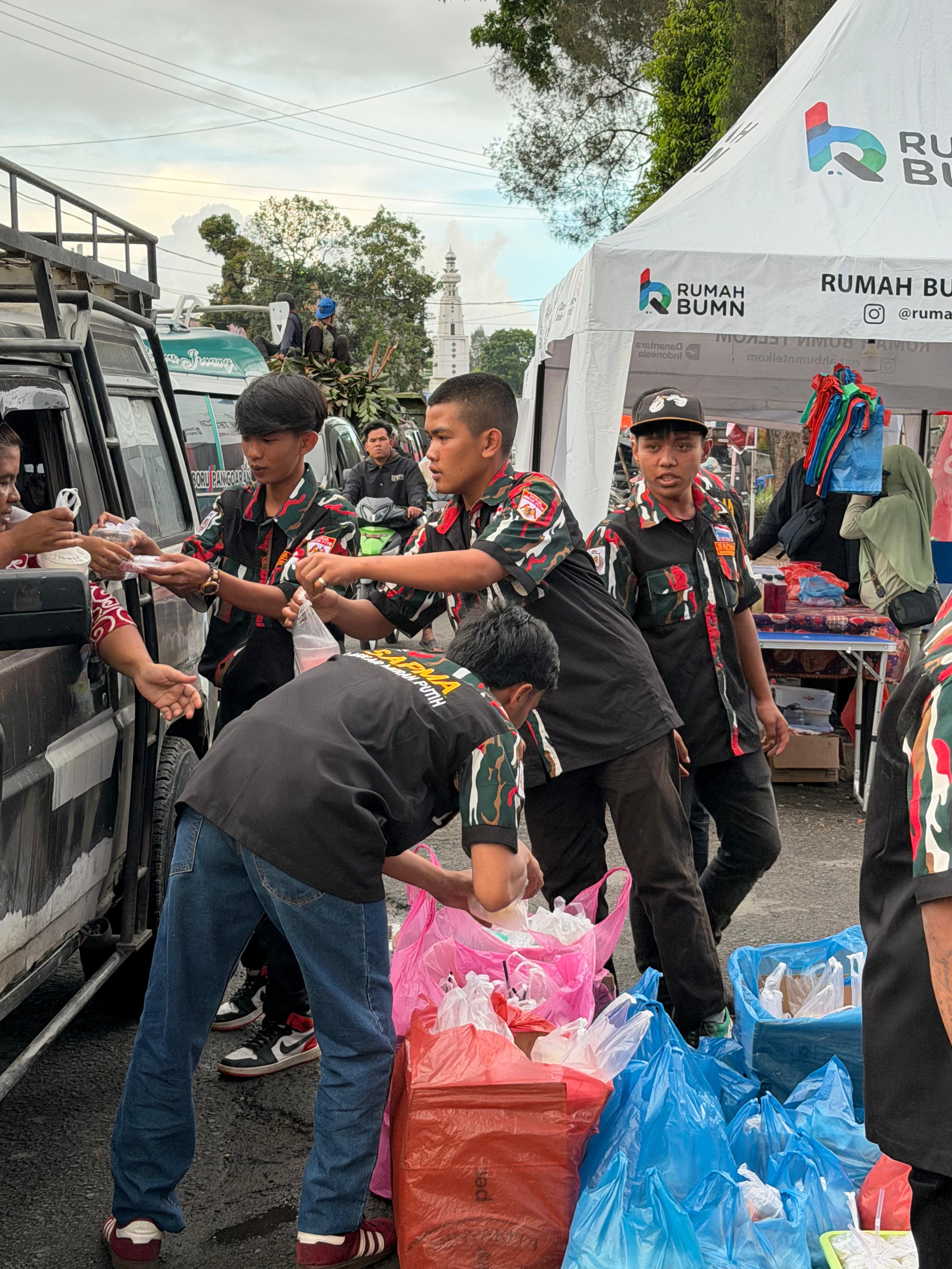 Anggota SAPMA LMP Karo membagikan takjil kepada pengguna jalan di Simpang Katepul, Kabanjahe, Minggu (15/3/2026), setelah memborong dagangan UMKM setempat.