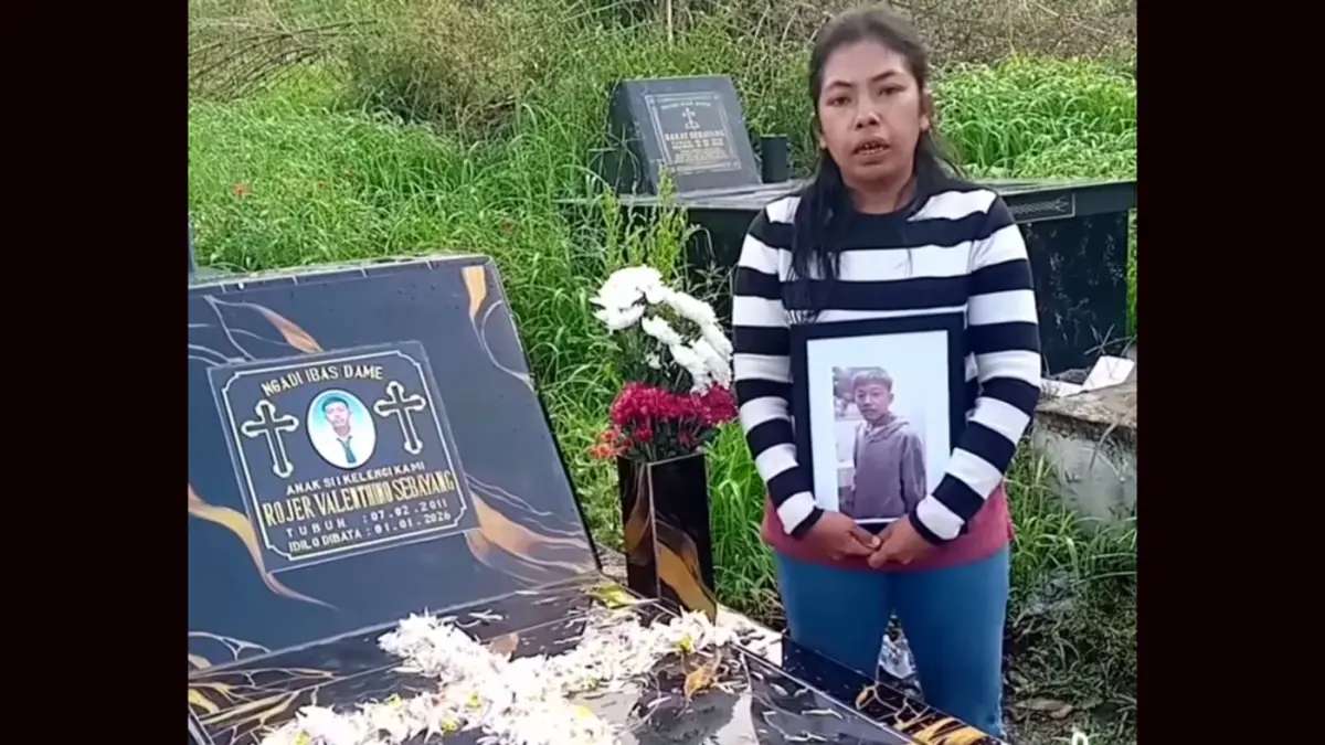 Ibu korban Rojer Sebayang menangis di makam anaknya sambil memegang foto dan meminta keadilan atas kasus penganiayaan yang belum tuntas.