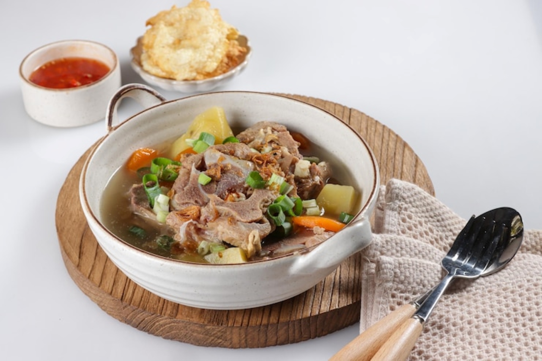 Ilustrasi. Sajian sop buntut sapi lengkap dengan emping dan sambal yang siap disantap. (freepik.com)