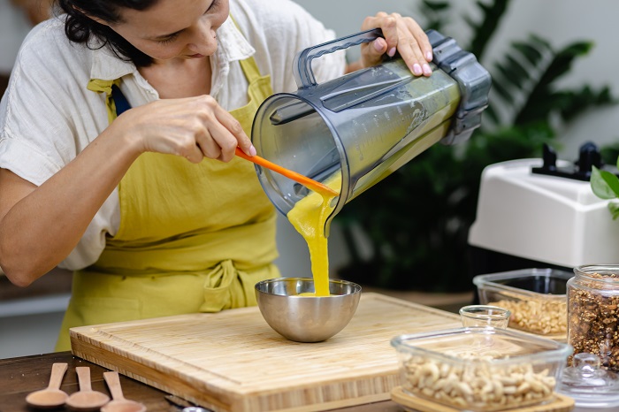 Ilustrasi seseorang menuang kunyit yang sudah dihaluskan menjadi bumbu dengan blender.