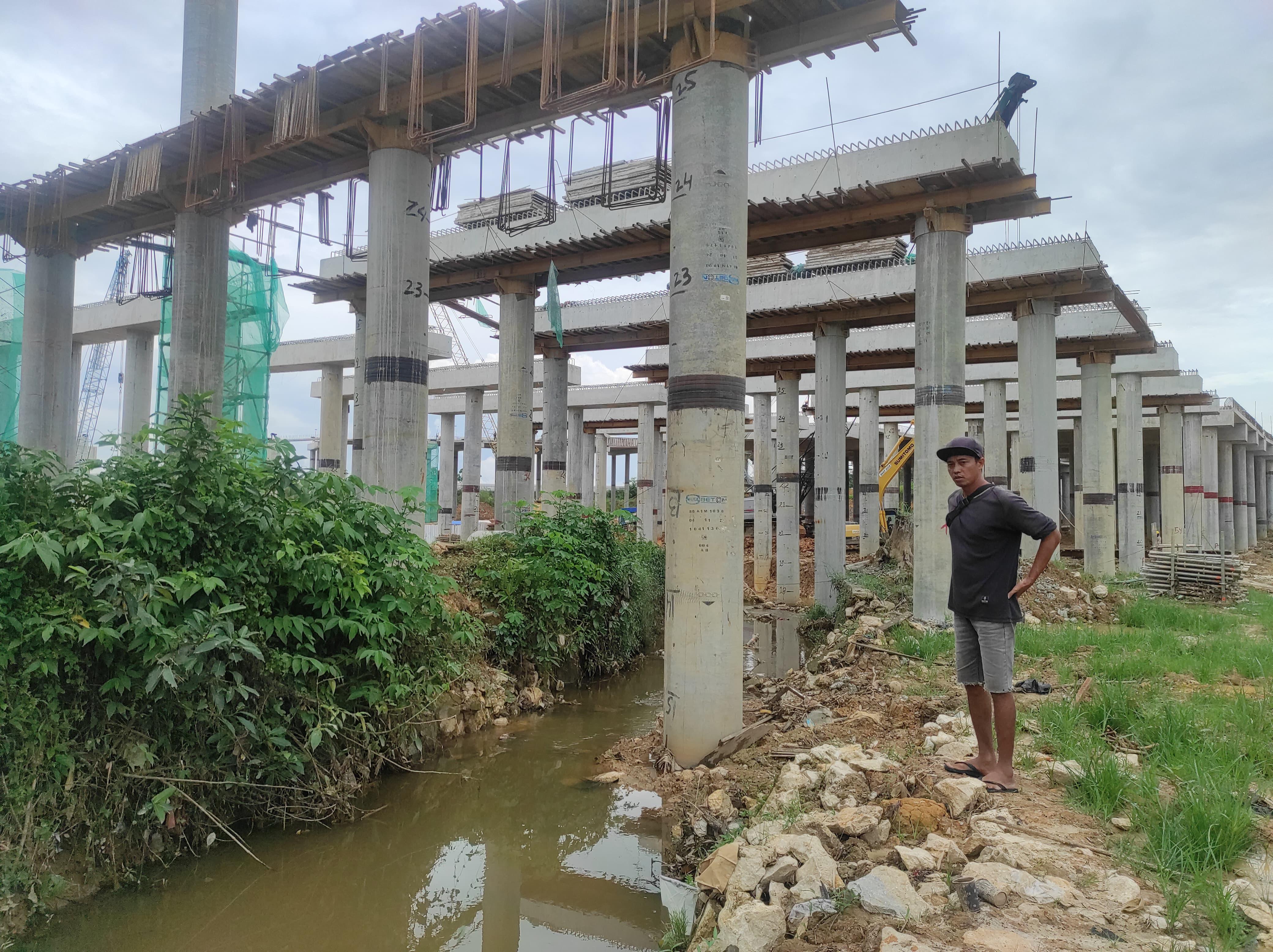 MEMINTA SOLUSI: Joko berdiri di dekat pancang Tol IKN yang ditengarai sebagai salah satu penyebab makin parahnya banjir di kawasan Karang Joang, Balikpapan.