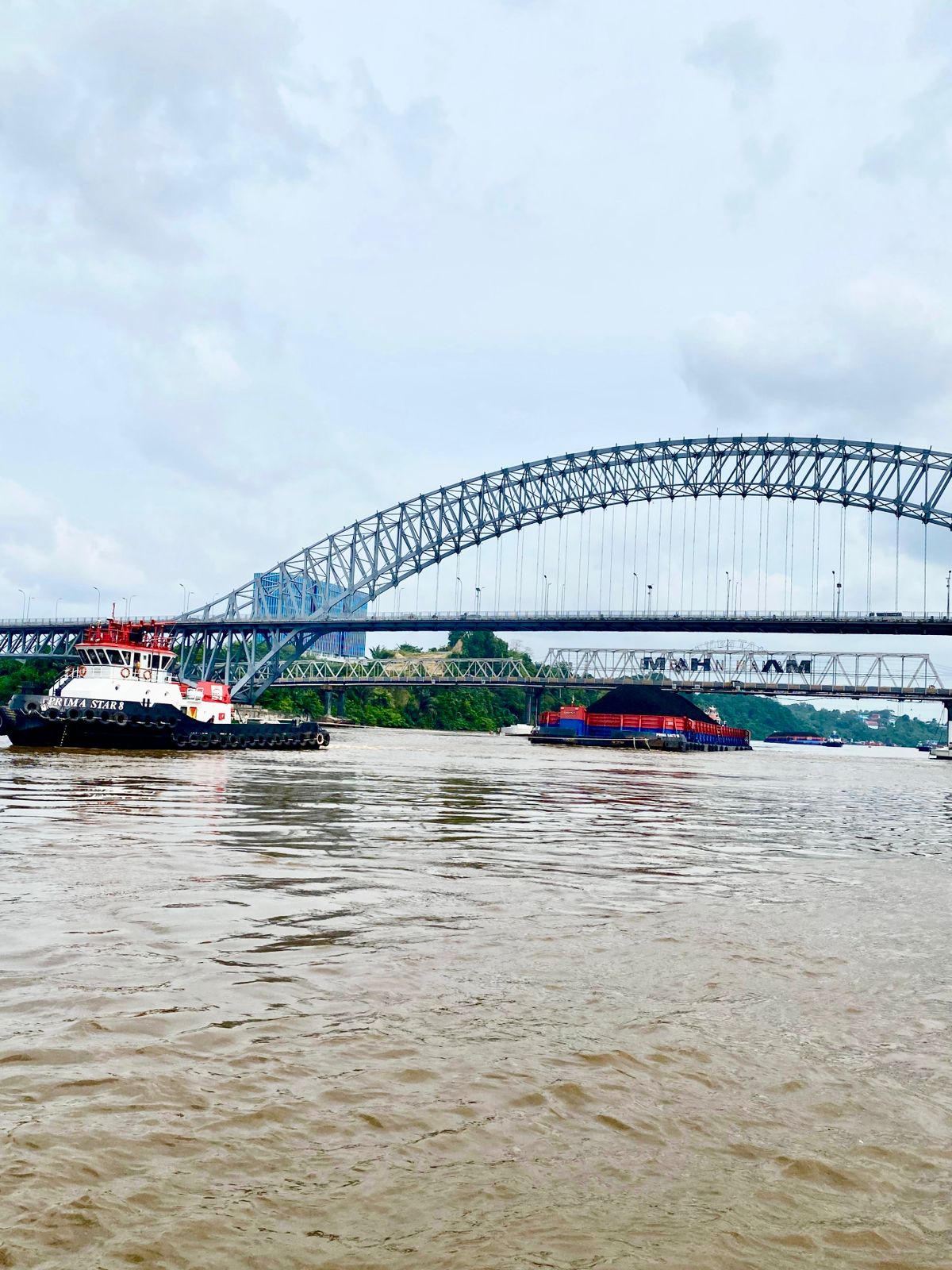 Kapal tongkang melintas di bawah Jembatan Mahkota II, Samarinda, dengan pengawalan kapal pandu Pelindo.