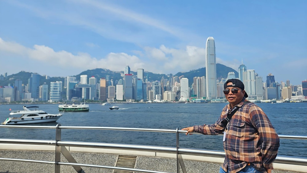 PELABUHAN VICTORIA: Andre Zaini dengan latar belakang keindahan Pelabuhan Victoria dengan air laut dan gedung-gedung pencakar langit.