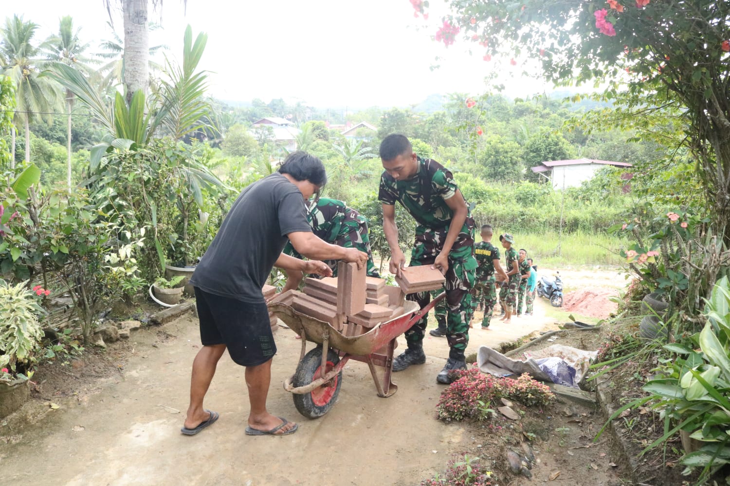 Personel Satgas TMMD ke-125 dan warga mengangkut batu bata dengan gerobak arko di Desa Suka Rahmat.
