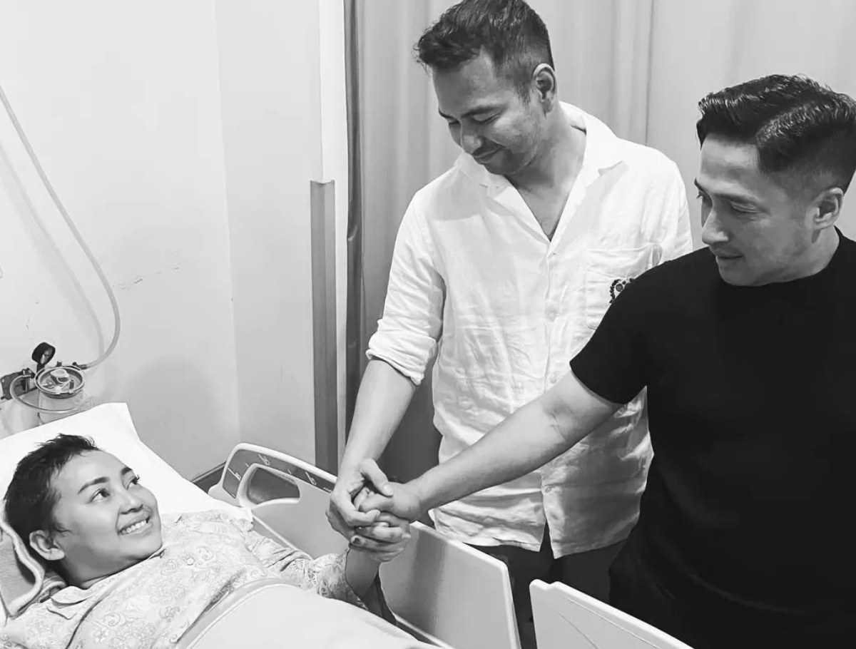 Mpok Alfa tersenyum hangat sambil dirawat di rumah sakit, ditemani Raffi Ahmad (kiri) dan Irfan Hakim (kanan) yang menyalami tangan sahabat mereka sebagai bentuk dukungan dan doa. (FOTO: IST)