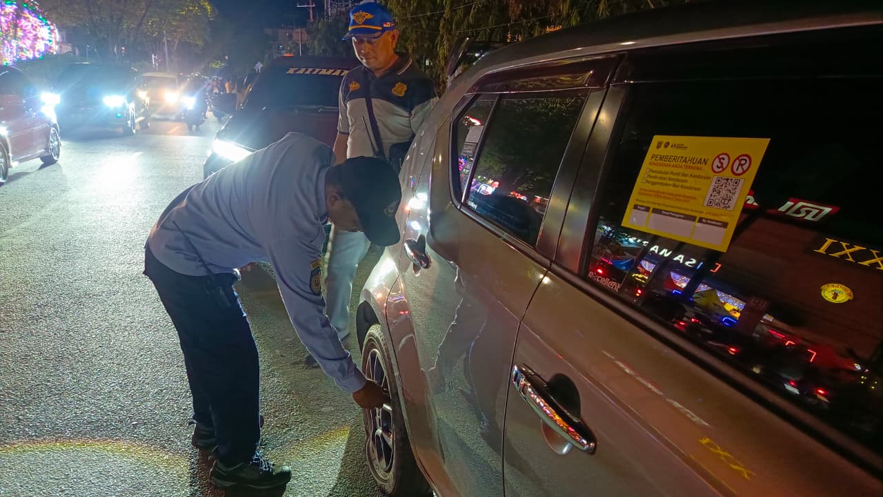 GEMBOSI: Petugas Dishub Samarinda menggembosi ban dan memasang stiker pelanggaran pada puluhan mobil yang parkir di bahu Jalan M Yamin, Kecamatan Samarinda Ulu, Minggu (15/11) malam.