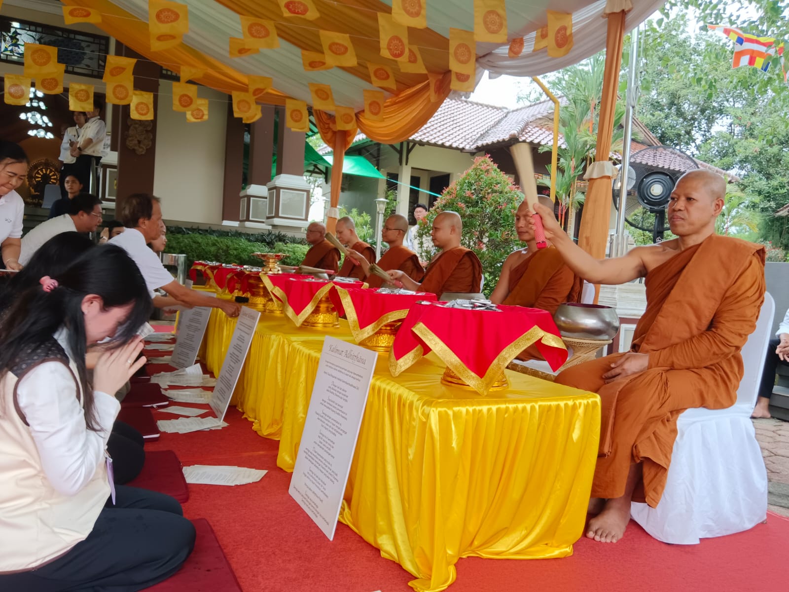 Tampak prosesi persembahan logam oleh umat yang disaksikan oleh para bhikkhu.