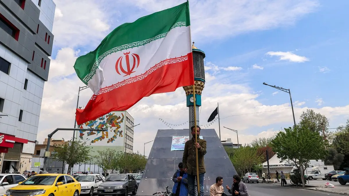 Seorang pria mengibarkan bendera Iran di persimpangan Valiasr Square di Teheran.