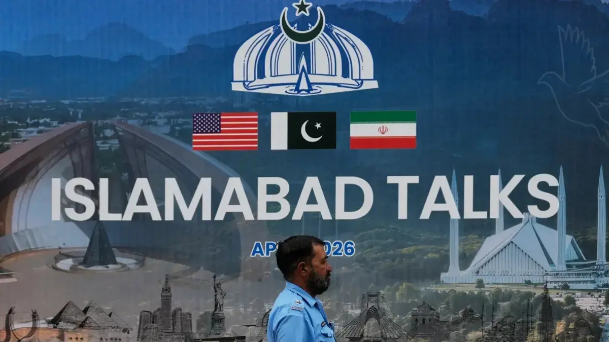Seorang petugas polisi berjalan melewati papan reklame mengenai negosiasi Amerika Serikat dan Iran, di luar pusat fasilitasi media di Islamabad, Pakistan, Sabtu, 11 April 2026. (AP Photo/Anjum Naveed)