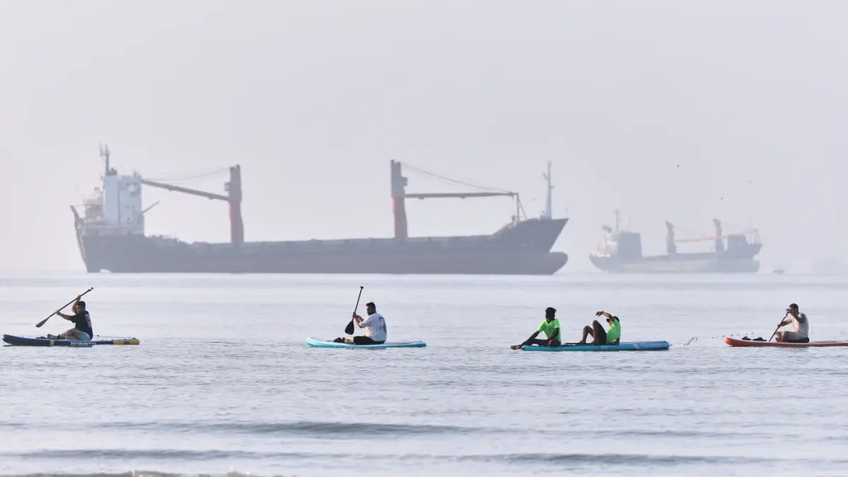 SELAT HORMUZ: Aktivitas warga mendayung di pesisir pantai dengan latar belakang deretan kapal kargo yang sedang bersandar di Selat Hormuz, kawasan Bandar Abbas, Iran, Senin (1/6/2026).(AP)
