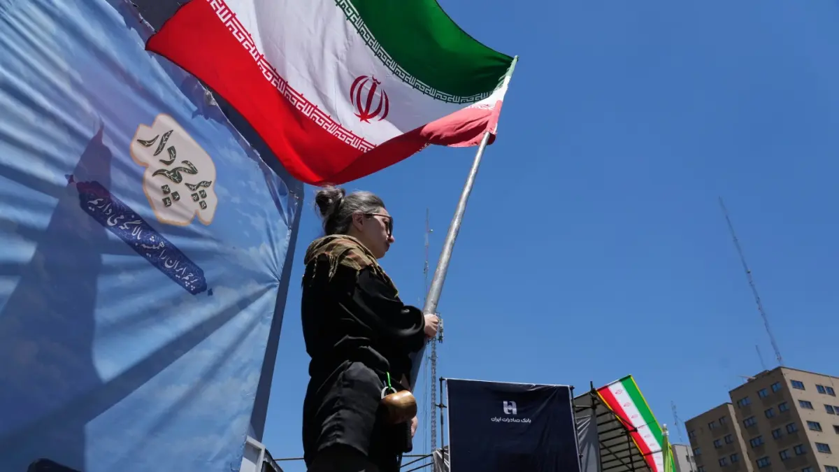 LAMBAIKAN: Seorang wanita melambaikan bendera Iran selama kampanye pro-pemerintah saat potret Pemimpin Tertinggi yang tewas pada 28 Februari, ditampilkan disebelah kanan, di pusat kota Teheran, Iran, Senin, 15 Juni 2026.(AP)