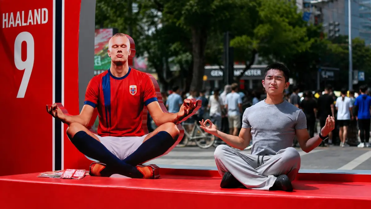 Seorang penggemar berpose di samping instalasi Erling Haaland di Beijing, mencerminkan melonjaknya popularitas sang striker usai Piala Dunia 2026. (GREG BAKER/AFP)