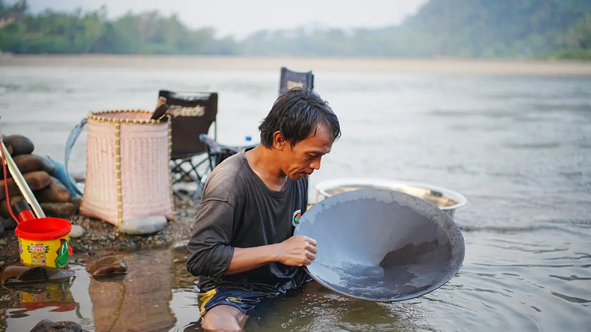 MENDULANG EMAS: Puput, seorang pencari emas tradisional, duduk memegang dulang hitam di air dangkal untuk memisahkan butiran emas dari pasir di bantaran Sungai Mahakam, kawasan Long Bagun Ilir, Kabupaten Mahakam Ulu (Mahulu). Puput menjadikan surutnya Sungai Mahakam sebagai mata pencaharian utamanya sejak kemarau melanda. Dari aktivitas mendulang sejak pagi hingga sore hari, ia mampu mengantongi rata-rata 500 milligram emas per hari yang dijual kepada pengepul seharga Rp1,9 juta per gram. (FOTO: JODY KRISTIANTO / KALTIM POST)