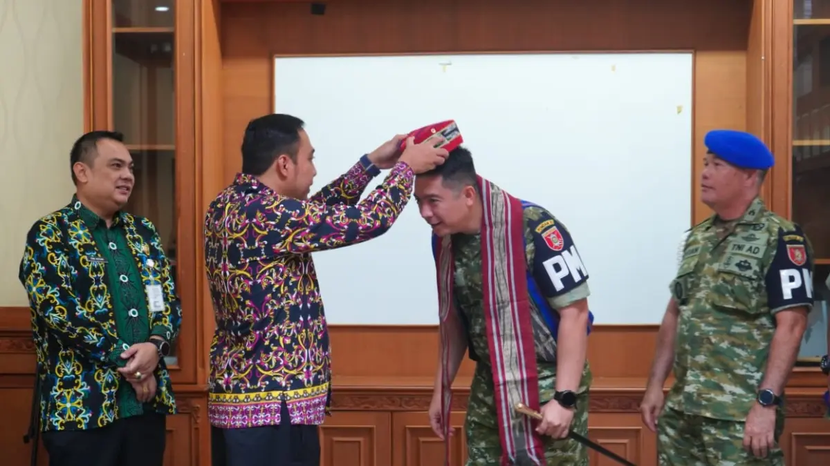 Bupati Kubar Frederick Edwin memasangkan songkok khas Kutai Barat kepada Dandenpom VI/1 Samarinda Letkol Cpm Muhammad Ade Wijaya.