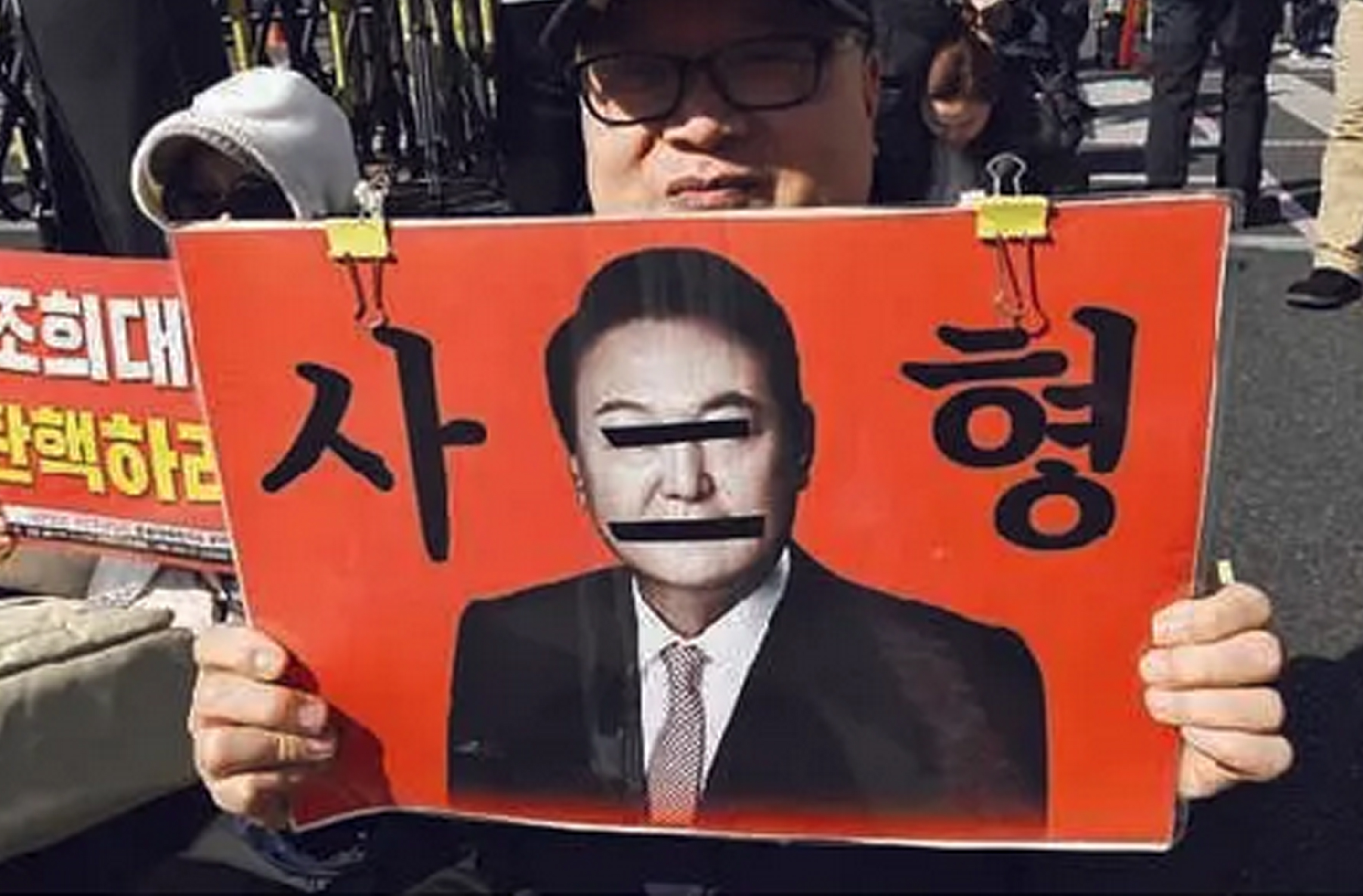 Pengunjuk rasa memegang poster dengan foto mantan presiden Yoon Suk-yeol bertuliskan "hukuman mati" di dekat Pengadilan Distrik Pusat Seoul.