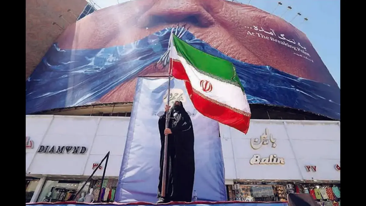 SIMBOL PERLAWANAN: Seorang perempuan memegang tiang bendera Iran di depan papan reklame anti-AS di Lapangan Valiasr, Teheran, Minggu (10/5). (AFP)
