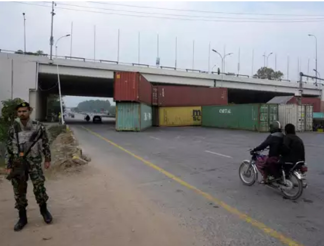 Seorang tentara berjaga ketika pengendara sepeda motor melaju di jalan raya, yang sebagian ditutup kontainer menjelang unjuk rasa para pendukung Imran Khan. (Foto: AP)