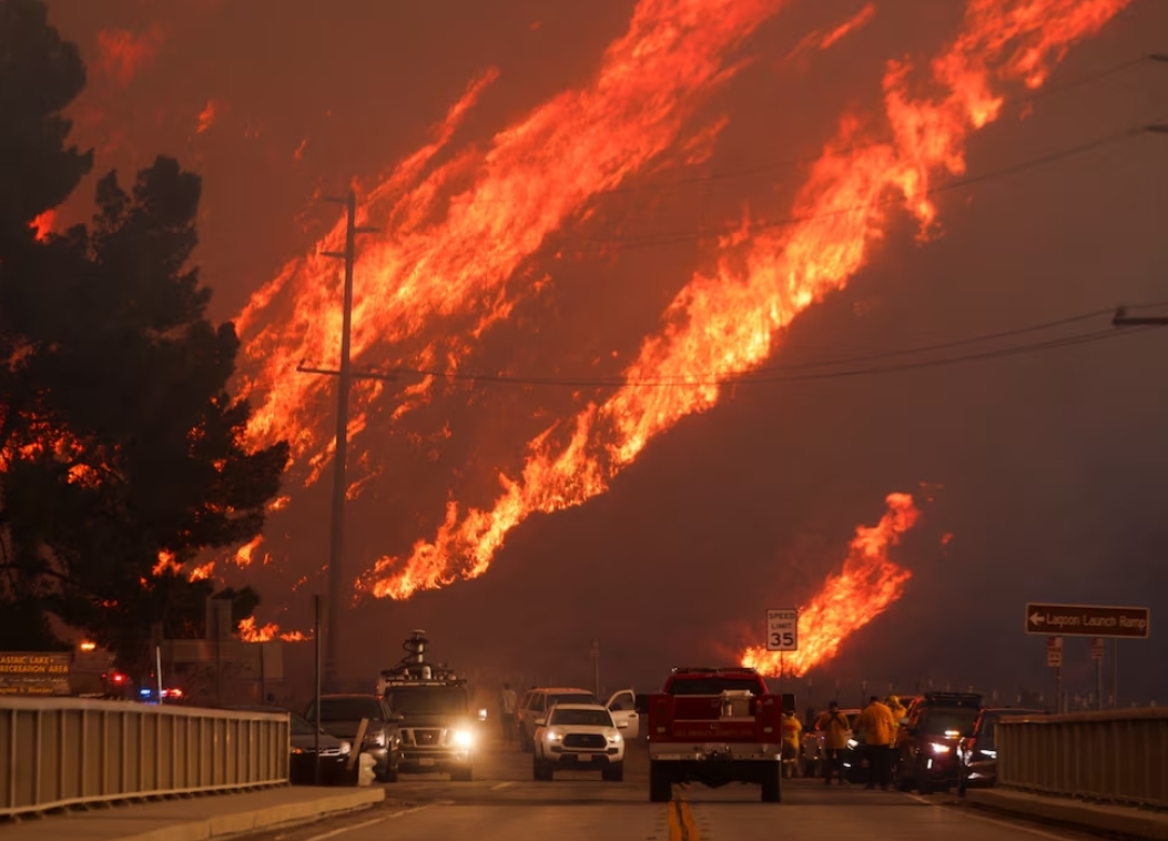 Api membubung di belakang kendaraan saat Kebakaran Hughes membakar Castaic Lake, California, 22 Januari. (REUTERS/David Swanson)
