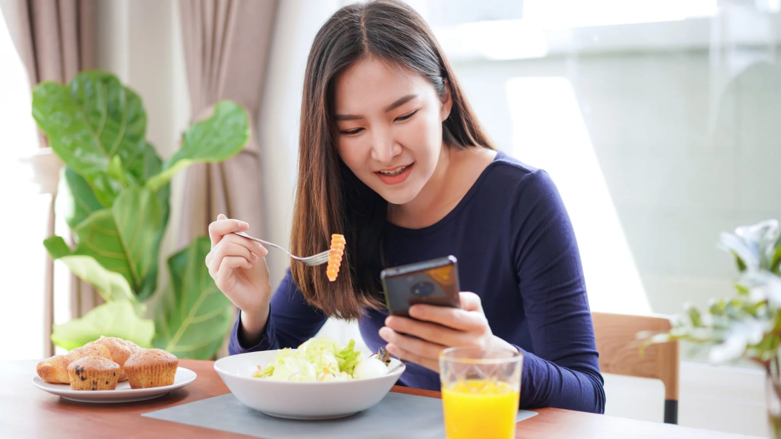 Ilustrasi orang yang sedang makan sambil menonton video di handphone.