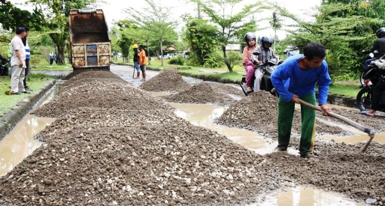 Pekerja dari Dinas Pekerjaan Umum Kota Pariaman menimbun jalan berlubang di kawasan Jembatan Muaro Pariaman menuju Desa Pauh Barat, Rabu siang (19/03/2025).