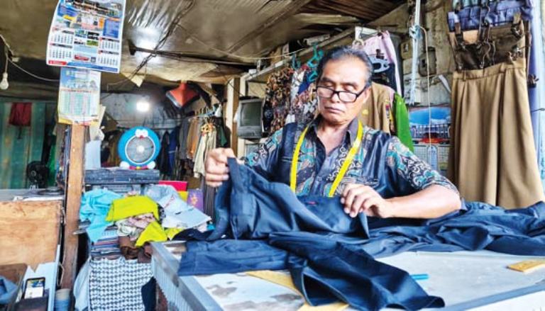 BERTAHAN: Marzeni pemilik Asli Tailor di Gedung Leter U Pasar Raya Padang tengah menuntaskan pesananan salah seorang pelanggannya, Minggu (29/6).(TANDRI EKA PUTRA/PADEK)