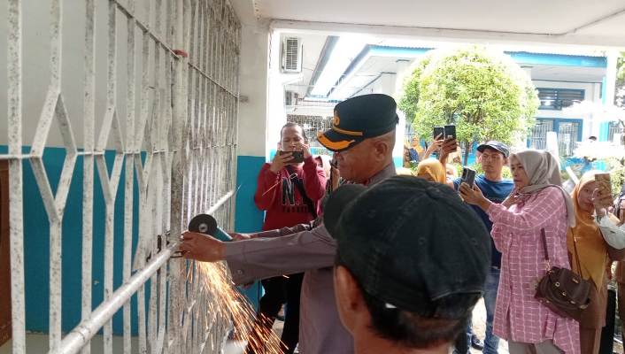 KARENA KECEWA: Kapolsek Kototangah Kompol Afrino Chaniago memotong rantai besi dan gembok yang menutupi akses masuk ke SMP Negeri 34 Padang kemarin (14/7). (DOKUMENTASI POLSEK KOTOTANGAH)