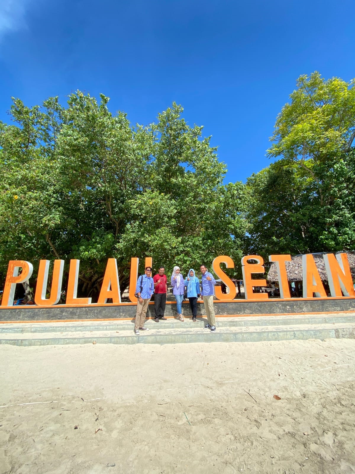 Wisatawan berfoto bersama dengan latar belakang tagline Pulau Setan.
