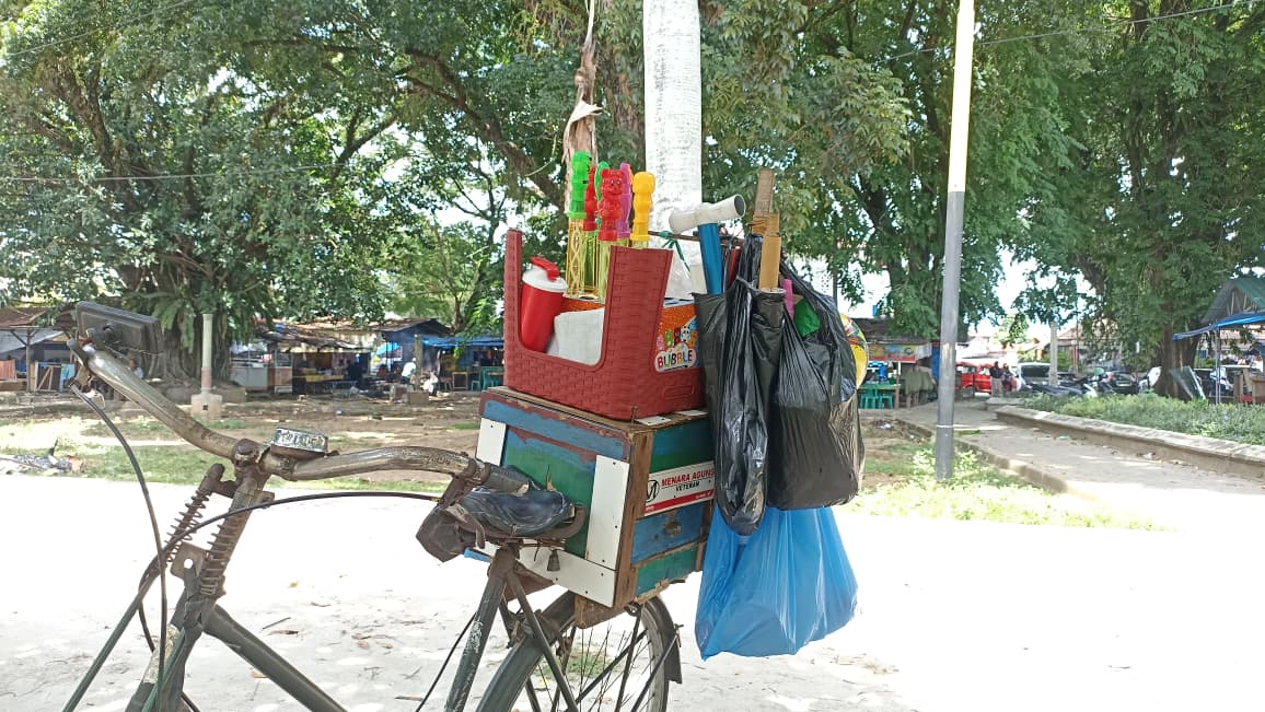 Di belakang sepeda Pak Nurman, bergoyang lembut aneka mainan berwarna cerah&mdash;mobil-mobilan, balon, dan kipas kecil&mdash;yang tergantung rapi di rak kayu.