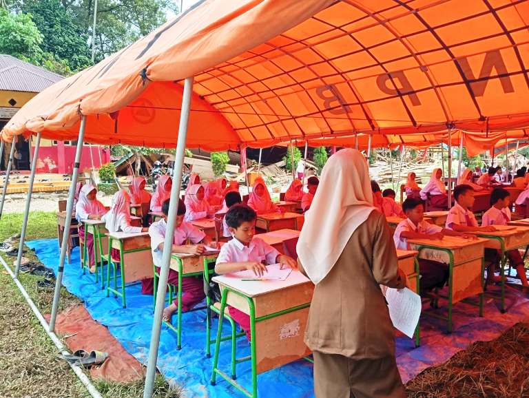 TAK MENYERAH: Para murid SDN 05 Batanganai tetap tekun menjalani ujian di bawah tenda BNPB di halaman sekolah itu, kemarin.