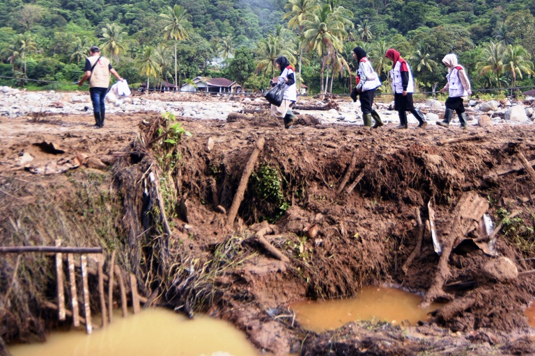 DIRUNDUNG BENCANA: Sejumlah relawan melintasi jalan berlumpur di Batubusuak, Kota Padang, Sabtu (13/12). Daerah itu berkali-kali dilanda banjir dalam beberapa pekan ini.