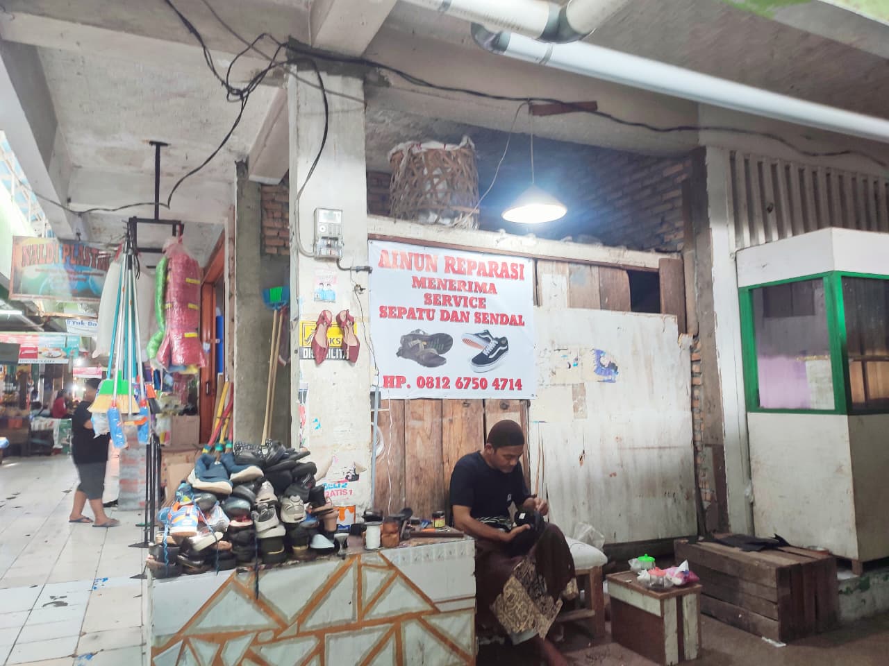 Marlius, tukang reparasi Sepatu di Pasar Alai, sedang memperbaiki sepatu langganannya, Minggu (4/1).