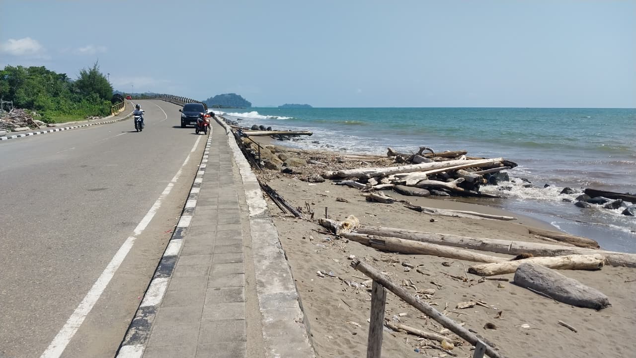 Pantai Lolong Belanti di Padang sepi saat Lebaran 2026. Tumpukan kayu sisa banjir menutup bibir pantai dan menghalangi wisatawan.