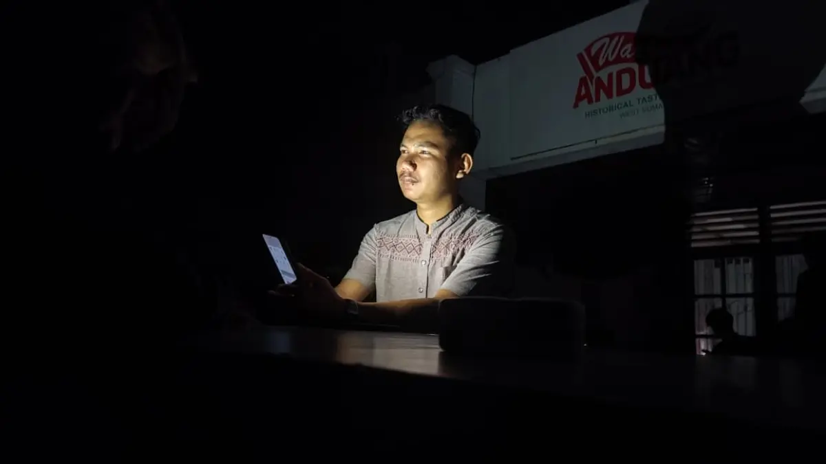 Warga Lolong Belanti Fardi (27) membuka handphone saat mati listrik pada Jumat (22/5/2026) pukul 19.45 WIB. (Randi/Padek)