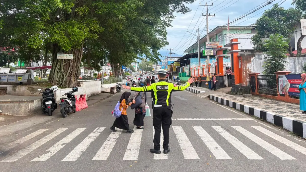 Personel Satlantas Polres Tanahdatar mengatur arus lalu lintas dan membantu pelajar menyeberang jalan di salah satu titik strategis Kota Batusangkar, Kamis (11/6), guna mengantisipasi kemacetan pada jam sibuk pagi. (DOK Polres Tanahdatar)