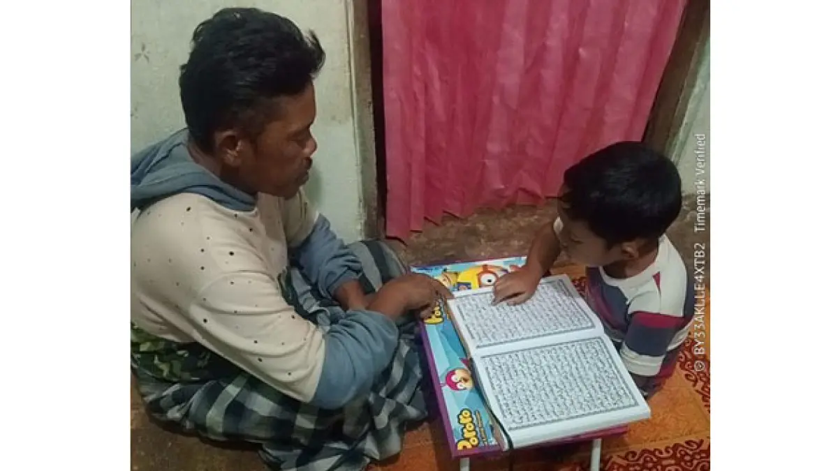Seorang ayah sedang mendampingi anaknya membaca Al Quran. Kegiatan ini bagian dari program SITI RABE di UPTD SD Negeri 12 Guguak VIII Koto. (TIM LAMAN GURU)