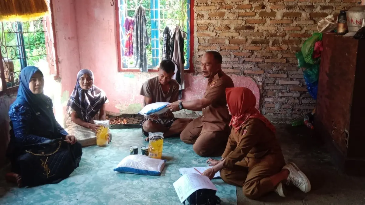 Kepala Bidang Rehabilitasi Sosial Dinas Sosial Kabupaten Agam Hasneril menyerahkan bantuan kebutuhan pokok kepada Aditya saat mengunjungi kediamannya, Selasa (14/7). DINSOS AGAM)