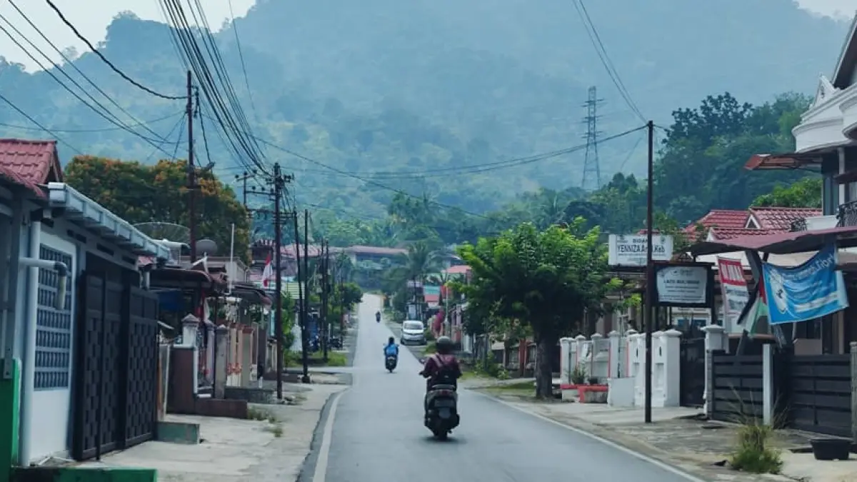 Tiga warga melintas menggunakan sepeda motor dengan latar perbukitan di Kota Padang saat kabut asap menyelimuti wilayah tersebut, Jumat (18/9/2026).