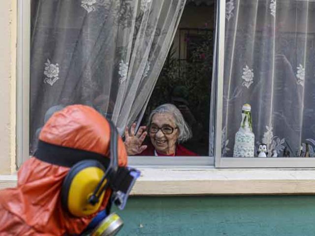 Seorang perempuan sepuh melambai kepada petugas disinfektan berbaju hazmat di Santiago, Cile. (AP Photo/Esteban Felix)