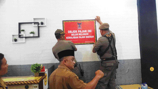 MENUNGGAK PAJAK: Petugas Bapenda Padang bersama Satpol PP memasang stiker menunggak pajak pada wajib pajak yang tidak mengindahkan kewajiban membayar pajak, kemarin.(IST)