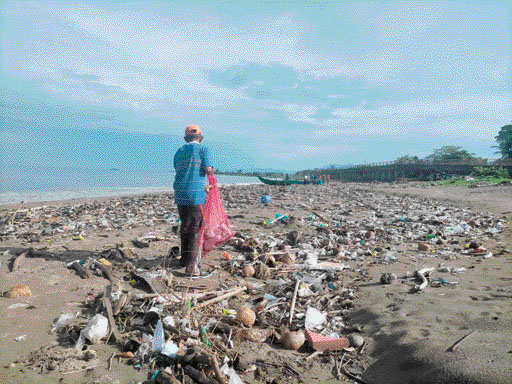 BERSERAKAN: Warga sedang berjalan di Pantai Padang yang dipenuhi sampah, kemarin.(KURNIA SANDI/PADEK)